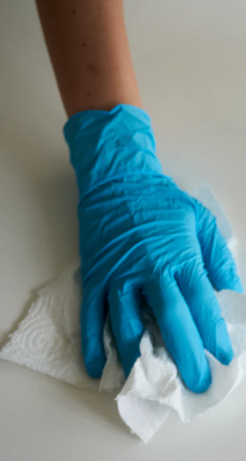 Hände in blauen Handschuhen wischen mit Küchenpapier eine helle Fläche ab